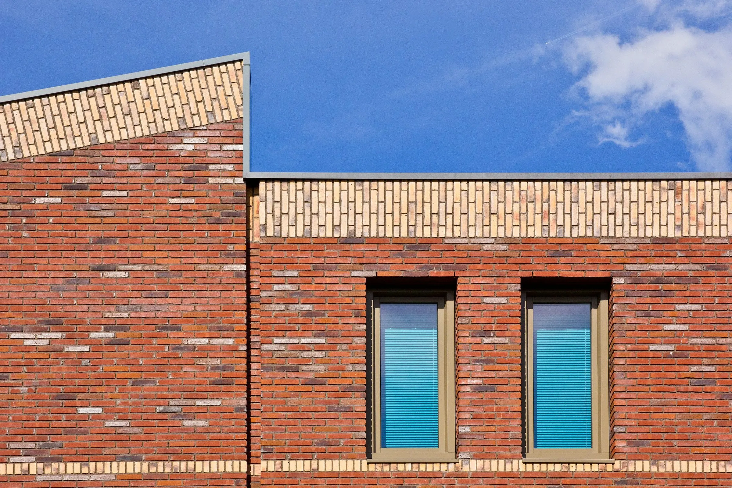 Detail of a contemporary brick facade with two deep-set windows against a blue sky