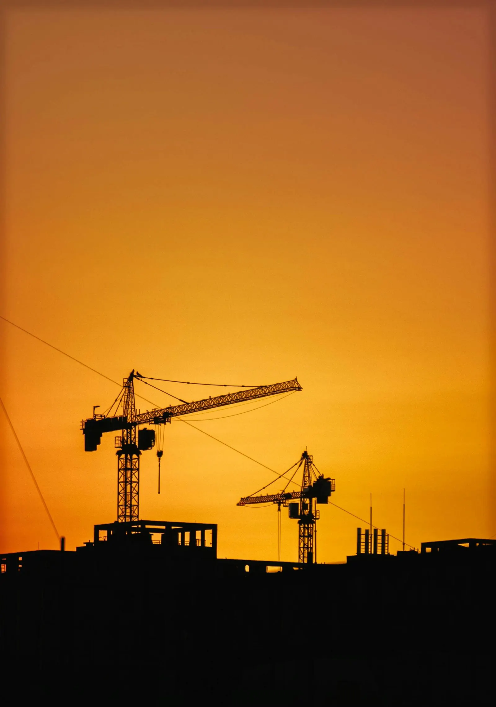 Two tower cranes silhouetted against an orange evening sky