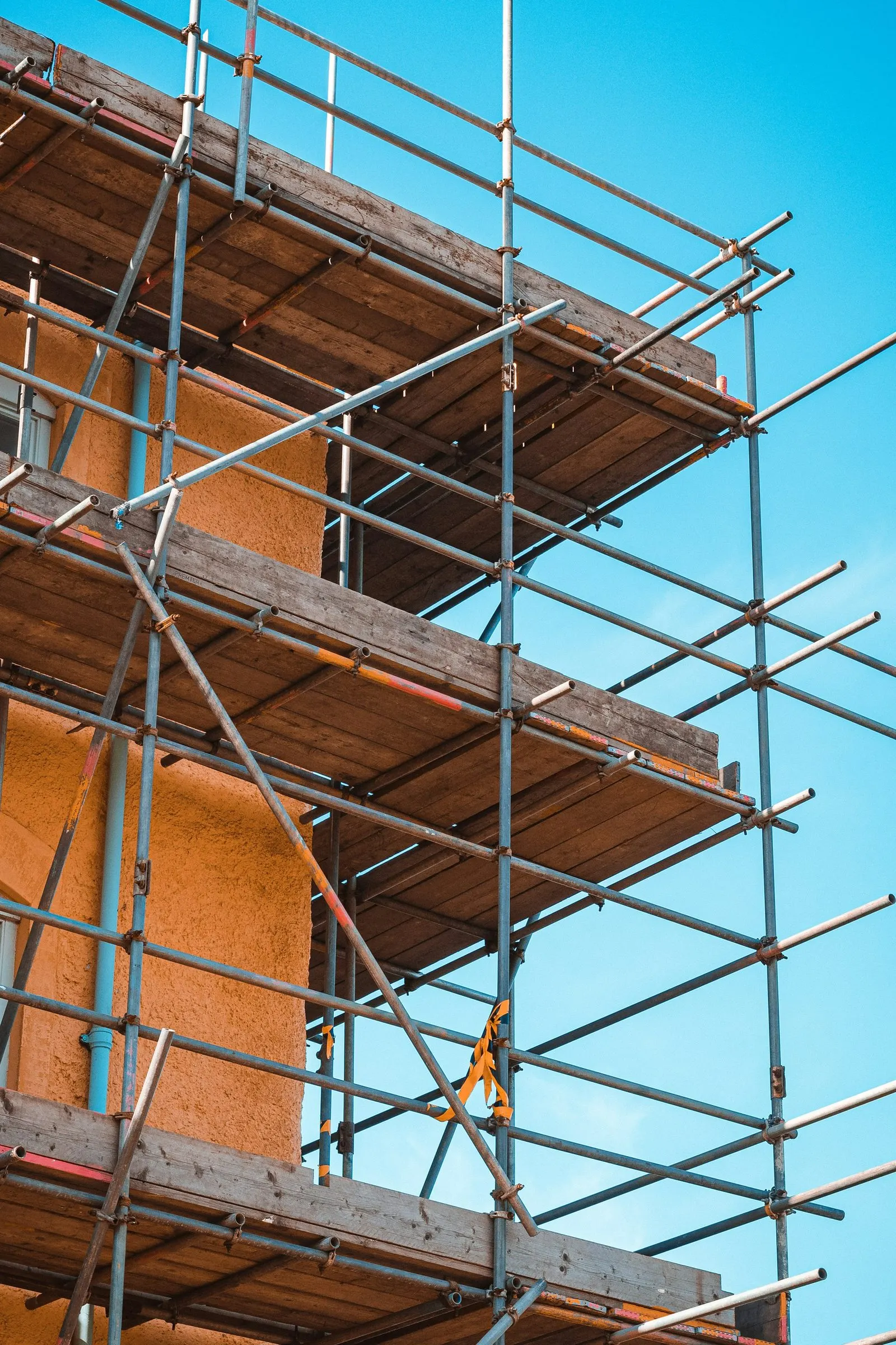 Scaffolding around the brickwork of a building under construction, against a blue sky